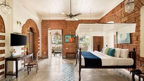 A room with a brick wall, a bed with a canopy, a television, and a desk with a chair. - Silva Heritage Resort Goa (Colva)