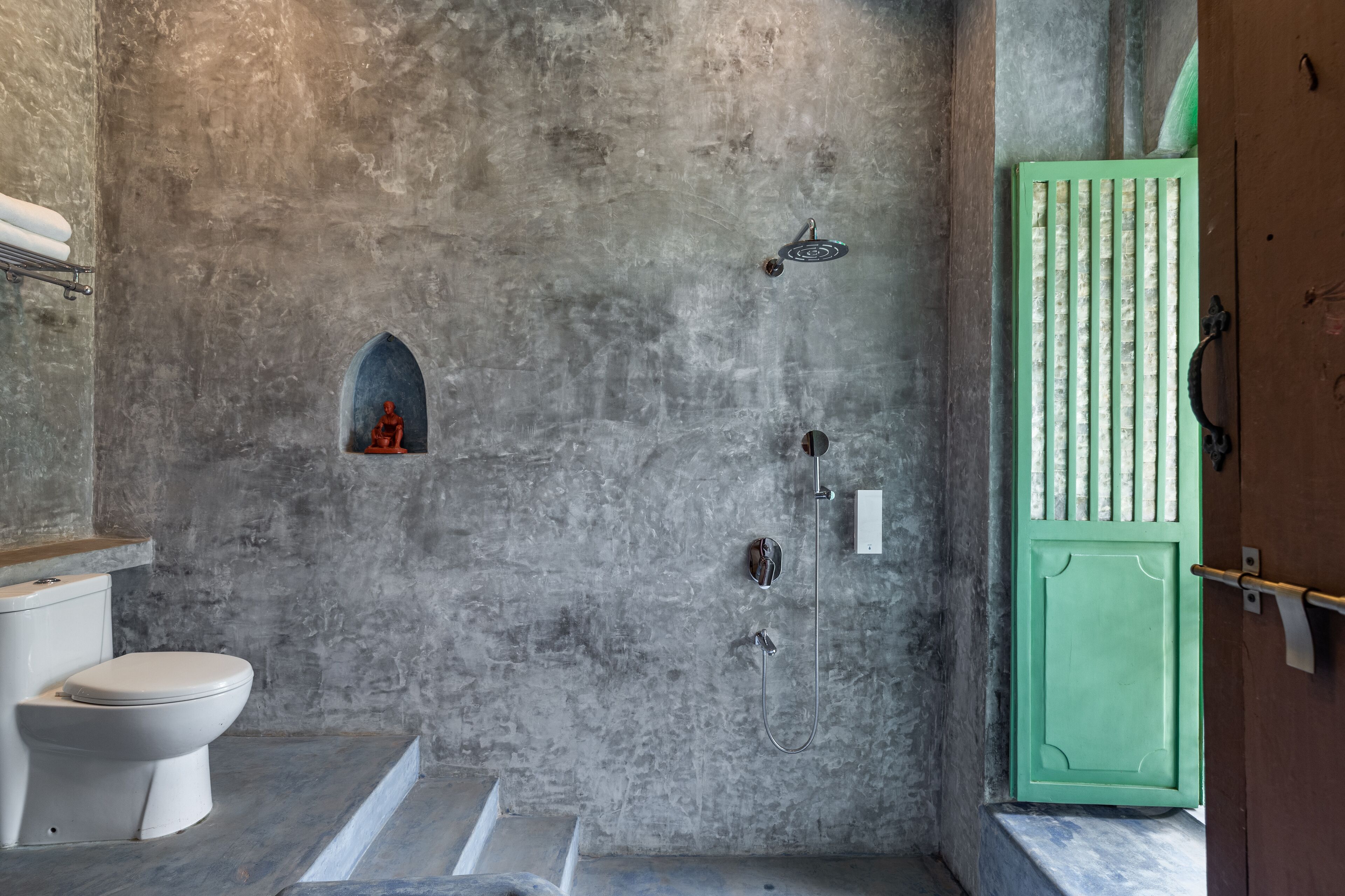 A bathroom with a concrete wall, a green door, a toilet, and a shower area.