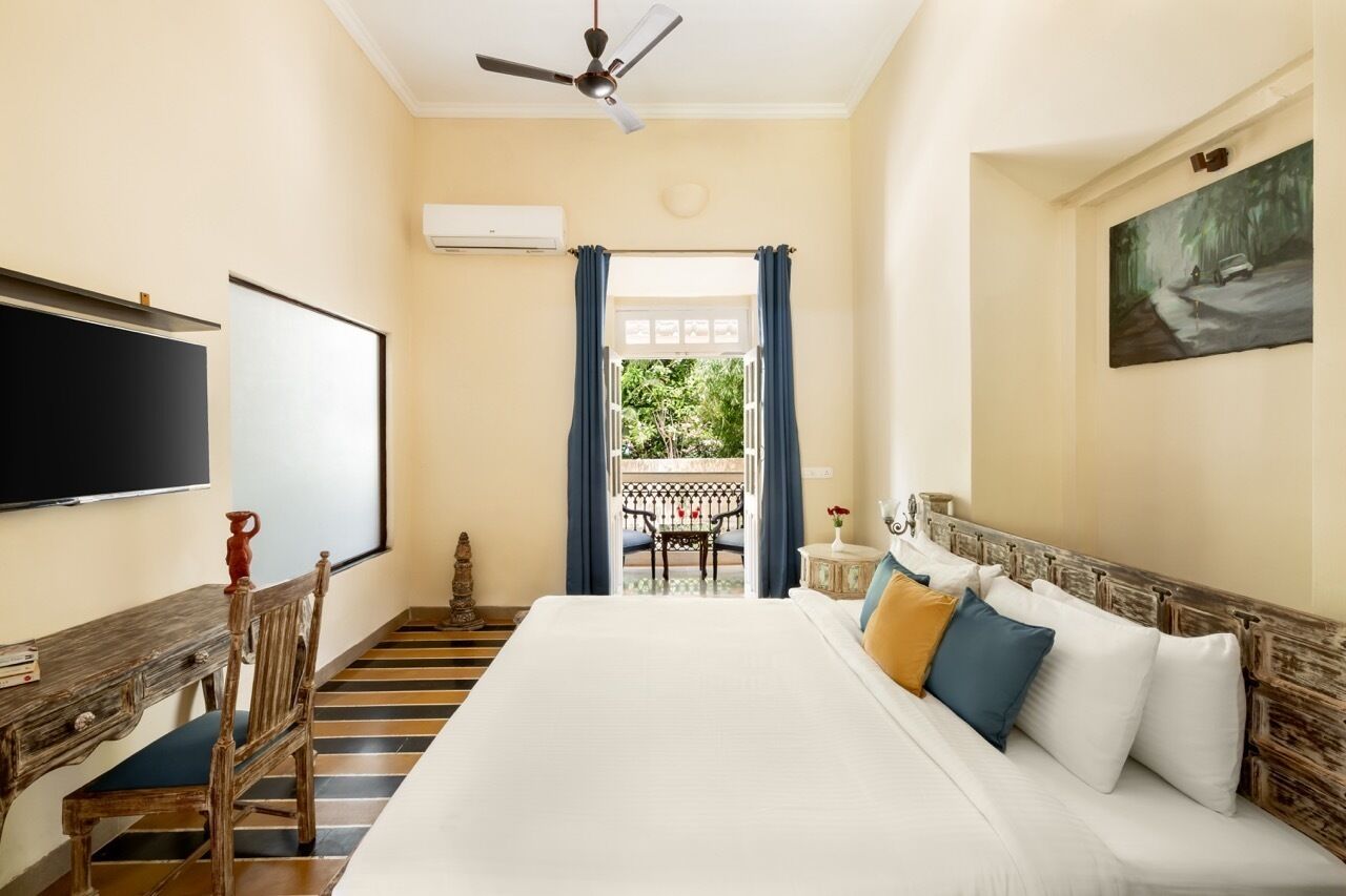 Habitación de hotel con una cama grande, un escritorio con silla, un ventilador de techo, un cuadro en la pared y vistas al exterior a través de una ventana.