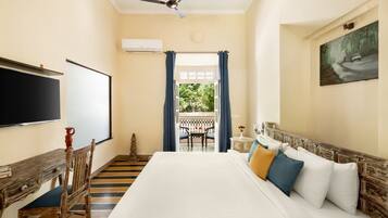 Habitación de hotel con una cama grande, un escritorio con silla, un ventilador de techo, un cuadro en la pared y vistas al exterior a través de una ventana.