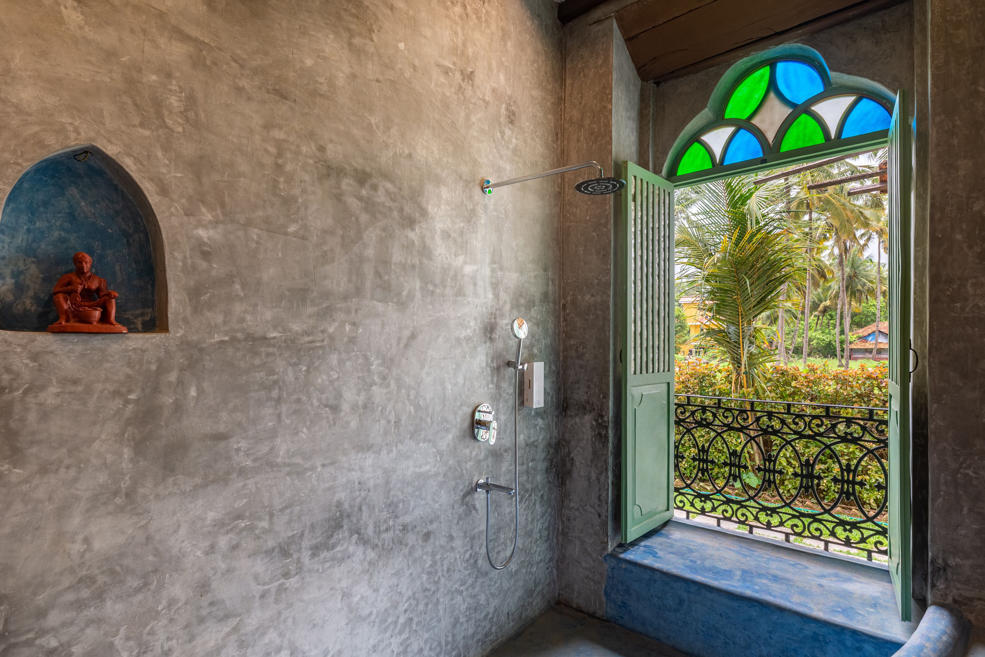 A bathroom with a shower, a decorative wall, and a view through a window with a green railing.