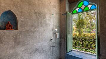 A bathroom with a shower, a decorative wall, and a view through a window with a green railing.
