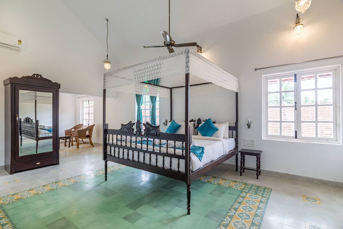 A four-poster bed with a canopy, a large mirror, a small table, and a view of the outside through a window.