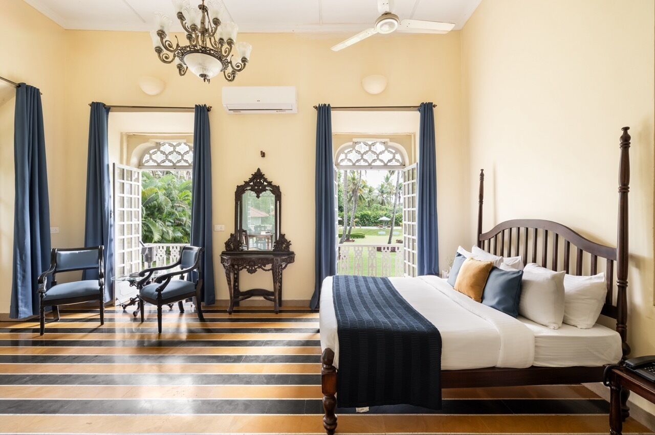 A bedroom with a bed, two chairs, a mirror, and a window with curtains.