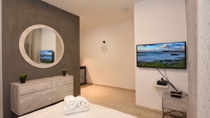 Ett modernt hotellrum med en stor säng, en rund spegel, en tv som är monterad på väggen och ett litet nattduksbord.