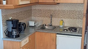 Une cuisine de taille réduite, dotée de meubles en bois, d’un réfrigérateur blanc, d’une machine à café et d’un évier.