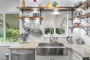 A kitchen with a stainless steel sink, wooden shelves, hanging pots, and a window with a view of greenery. - NEW! Dual next door units (2/1 & 1/1) - walk to downtown LW - 1.3mi to beach! (Lake Worth)