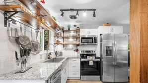 Une cuisine moderne dotée d’appareils électroménagers en acier inoxydable, d’un plan de travail en granit et d’étagères en bois.