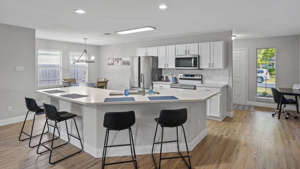 A modern kitchen with a central island, bar stools, and a dining area with a table and chairs.