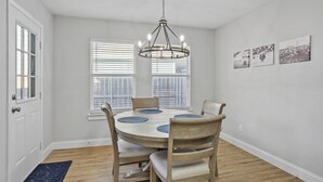 A dining room with a round table, four chairs, a chandelier, and three wall-mounted pictures.