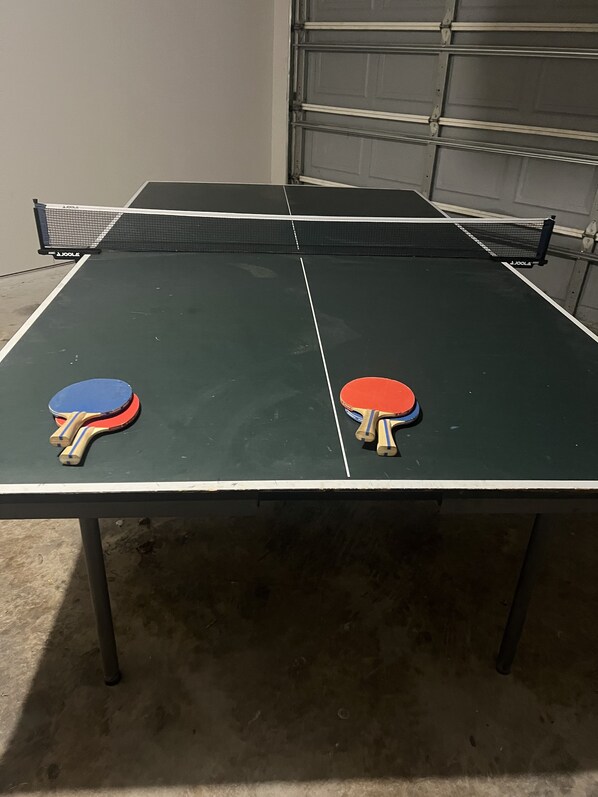 A ping pong table with two paddles on each side, set against a garage door.