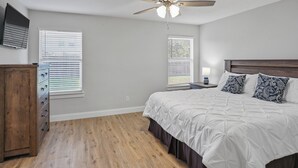 A bedroom with a bed, wooden dresser, ceiling fan, and two windows with blinds.