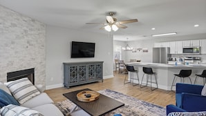 A modern living room with a fireplace, a dining area, and a kitchen with bar stools.