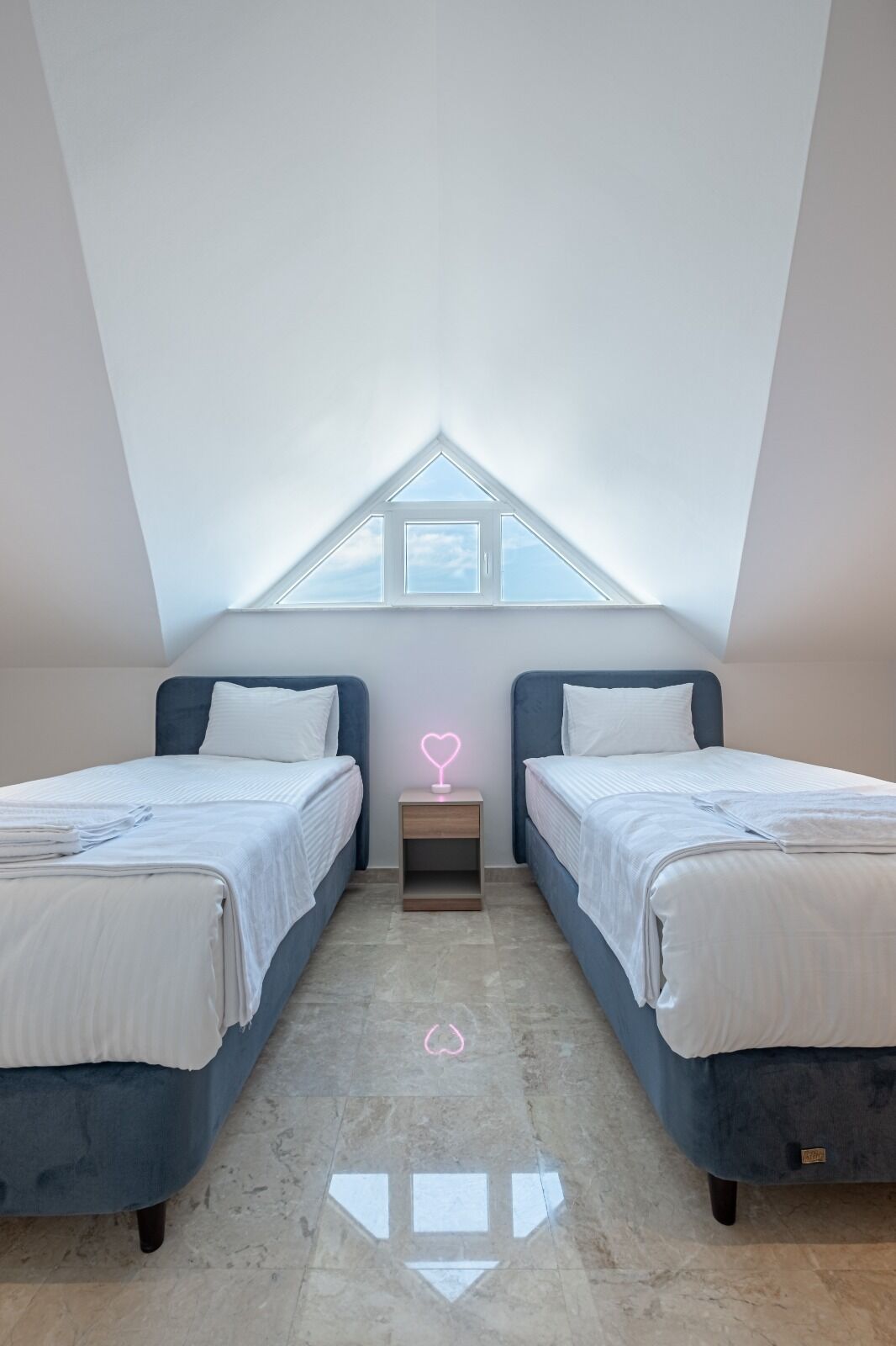 A bedroom with two beds, a skylight, and a neon heart decoration.