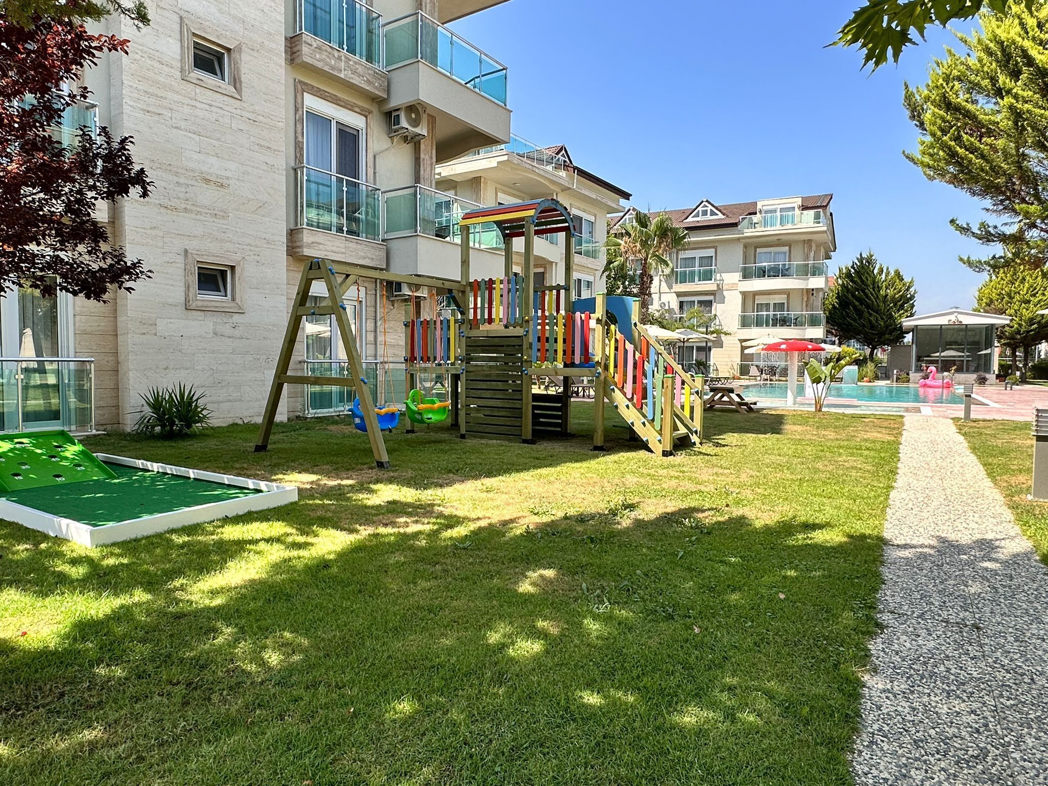 Ein Kinderspielplatz mit Rutsche und Schaukeln, ein kleines Schwimmbecken und ein Tennisplatz.