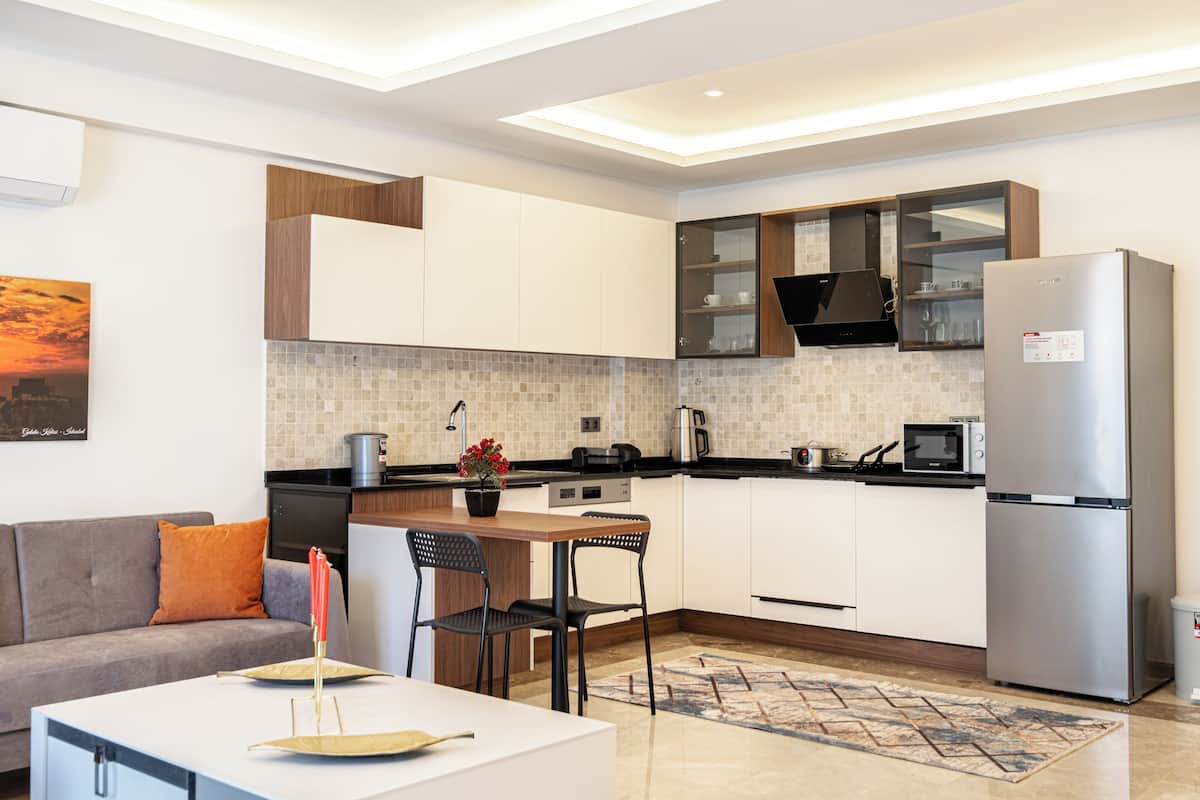 A modern kitchen with white cabinets, a stainless steel refrigerator, and a dining area with a table and chairs.