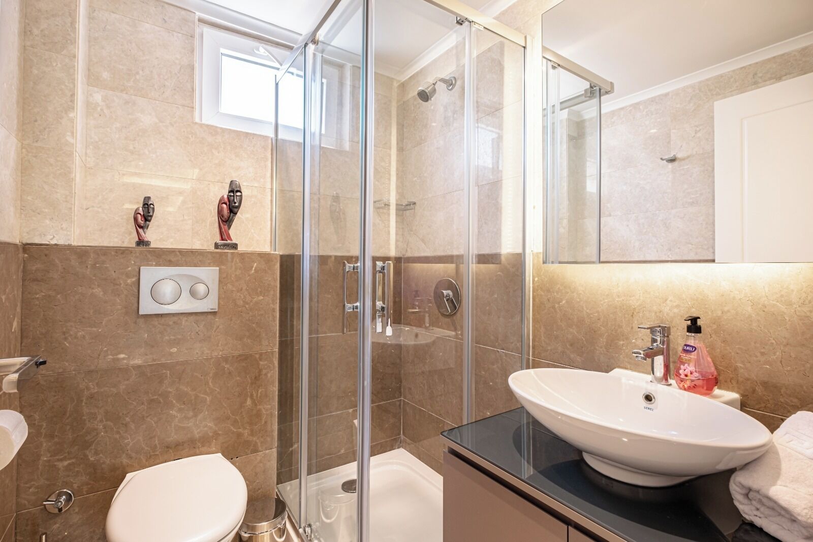 A modern bathroom with a glass-enclosed shower, a white sink with a black countertop, and a toilet.