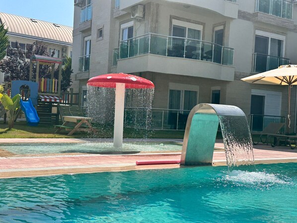 A swimming pool with a water fountain feature, a slide, and a children's play area.