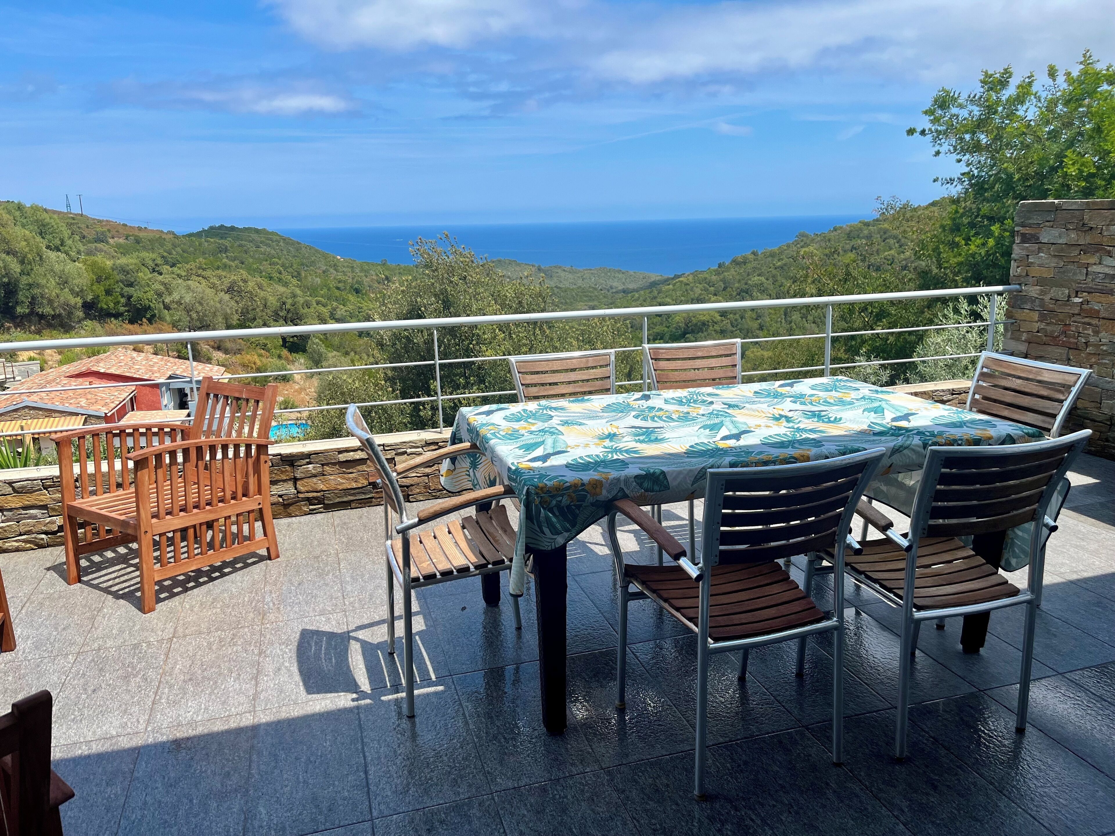 A terrace with a table and chairs, overlooking a scenic view of hills and the sea.