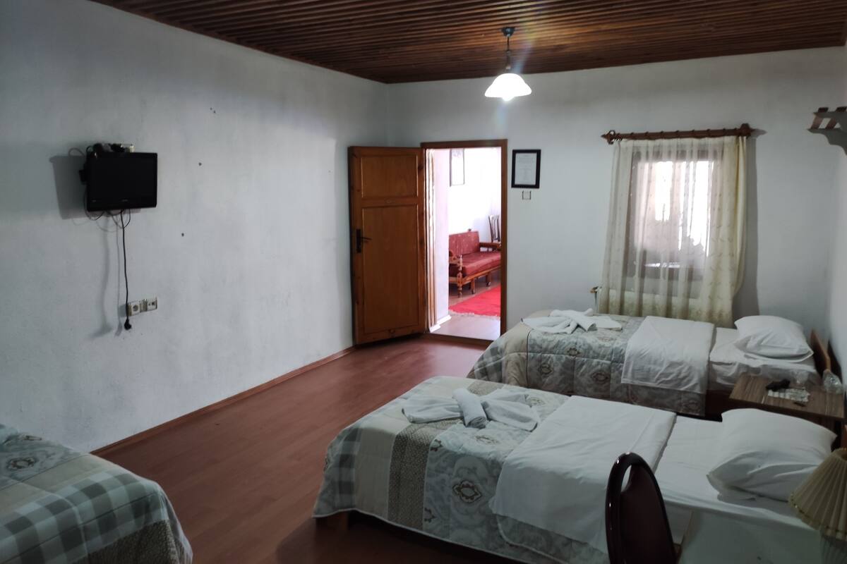 Ein Hotelzimmer mit zwei Betten, einer Holzbalkendecke, einem an der Wand befestigten Fernseher und einer Tür zu einem anderen Raum.