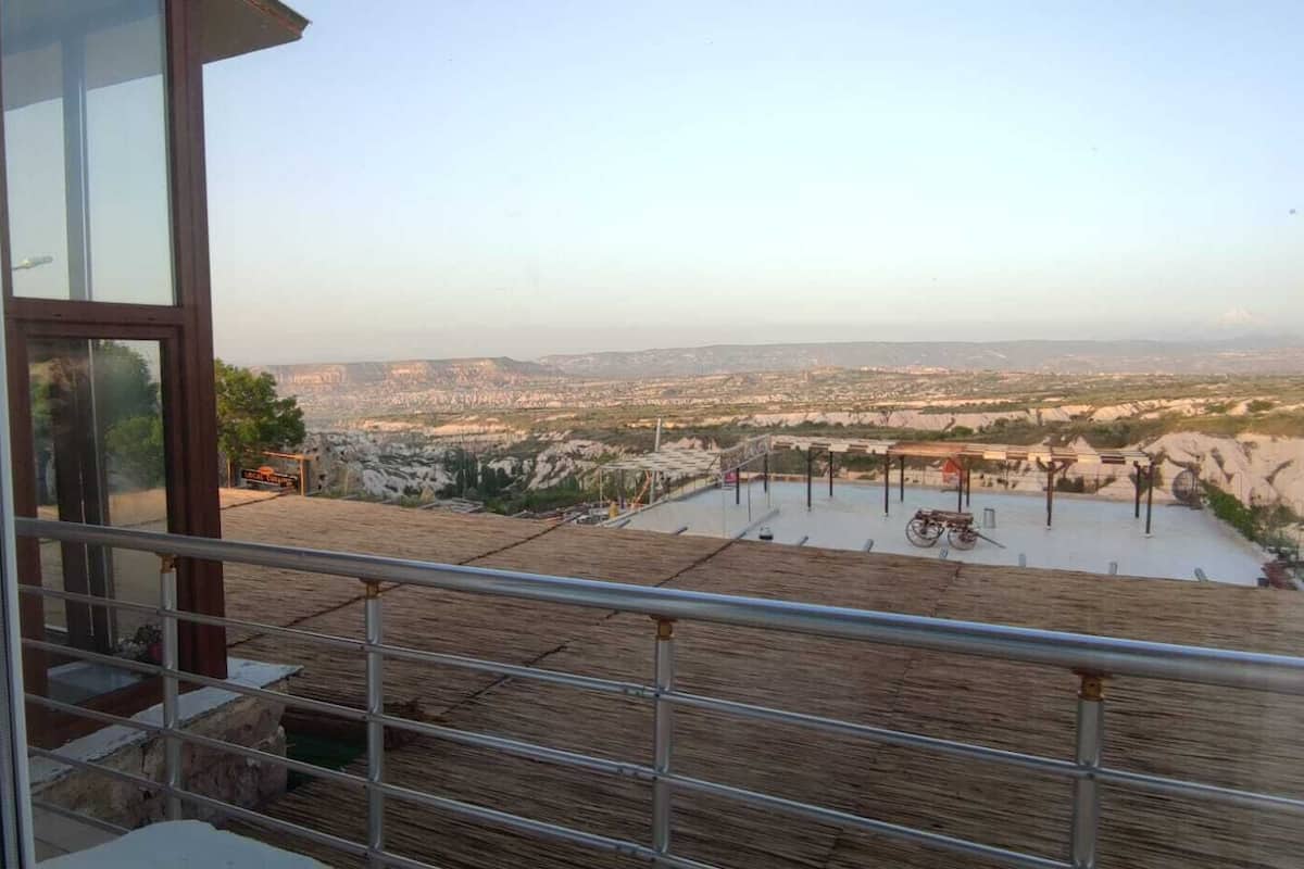 Ein Balkon mit Metallgeländer, der auf eine Landschaft mit einer entfernten Stadtansicht und blauem Himmel blickt.