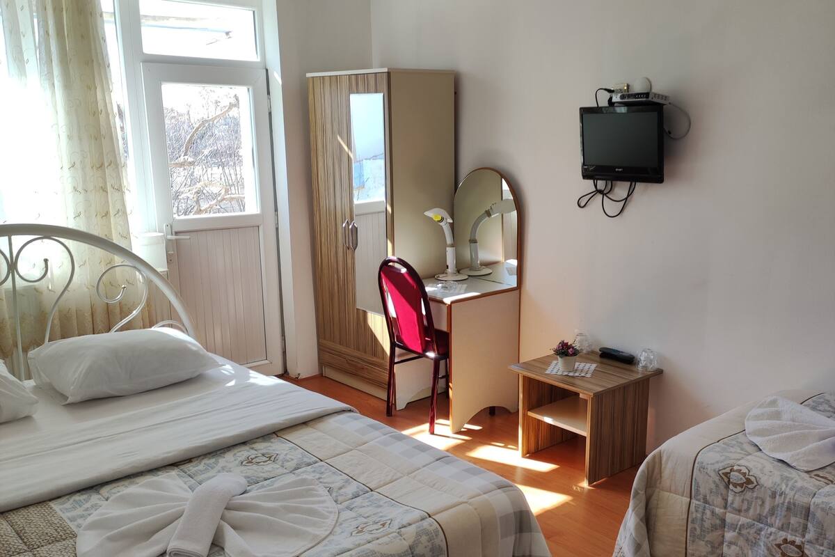 Ein Schlafzimmer mit zwei Betten, einem Schreibtisch mit Computer, einem Stuhl und einem Fenster mit Vorhängen.