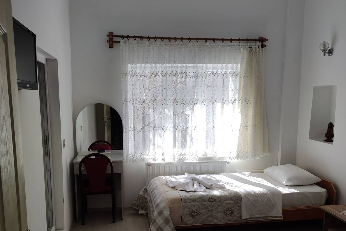 Ein Schlafzimmer mit zwei Betten, einem Schreibtisch, einem Stuhl, einem Spiegel und einem Fenster mit Spitzenvorhängen.