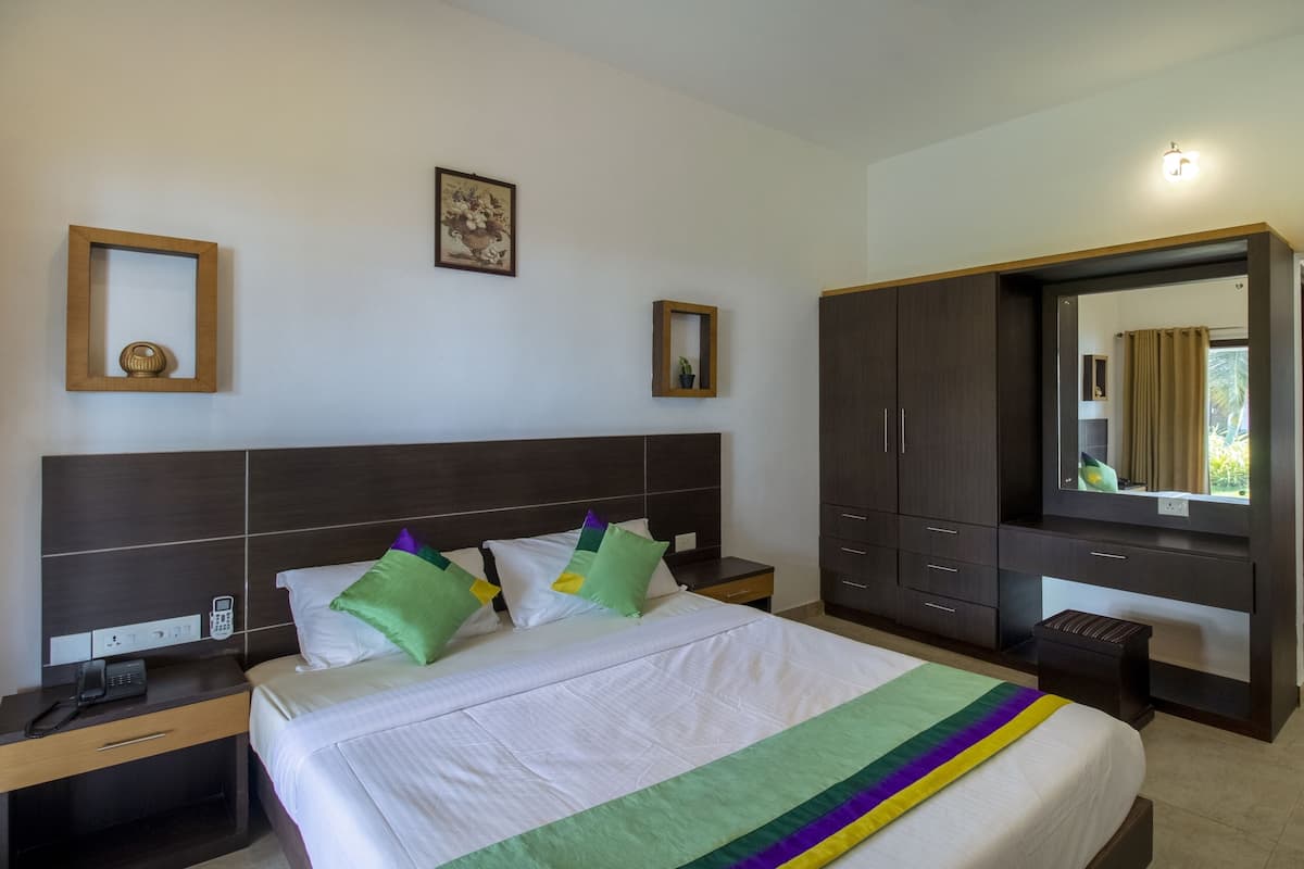 Quarto de hotel com uma cama grande, mesa de cabeceira com telefone, guarda-roupa, espelho e uma pequena janela com cortinas.