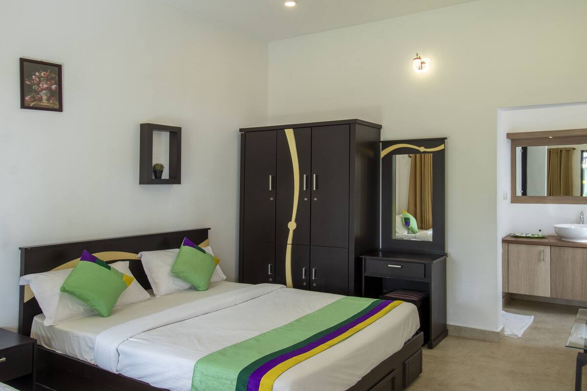 Quarto com cama, guarda-roupa, espelho, mesa de cabeceira e banheiro com pia e espelho.