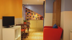 Un espace de vie compact comprenant un téléviseur, un coin repas, une cuisine avec un crédence colorée et une chaise rouge.