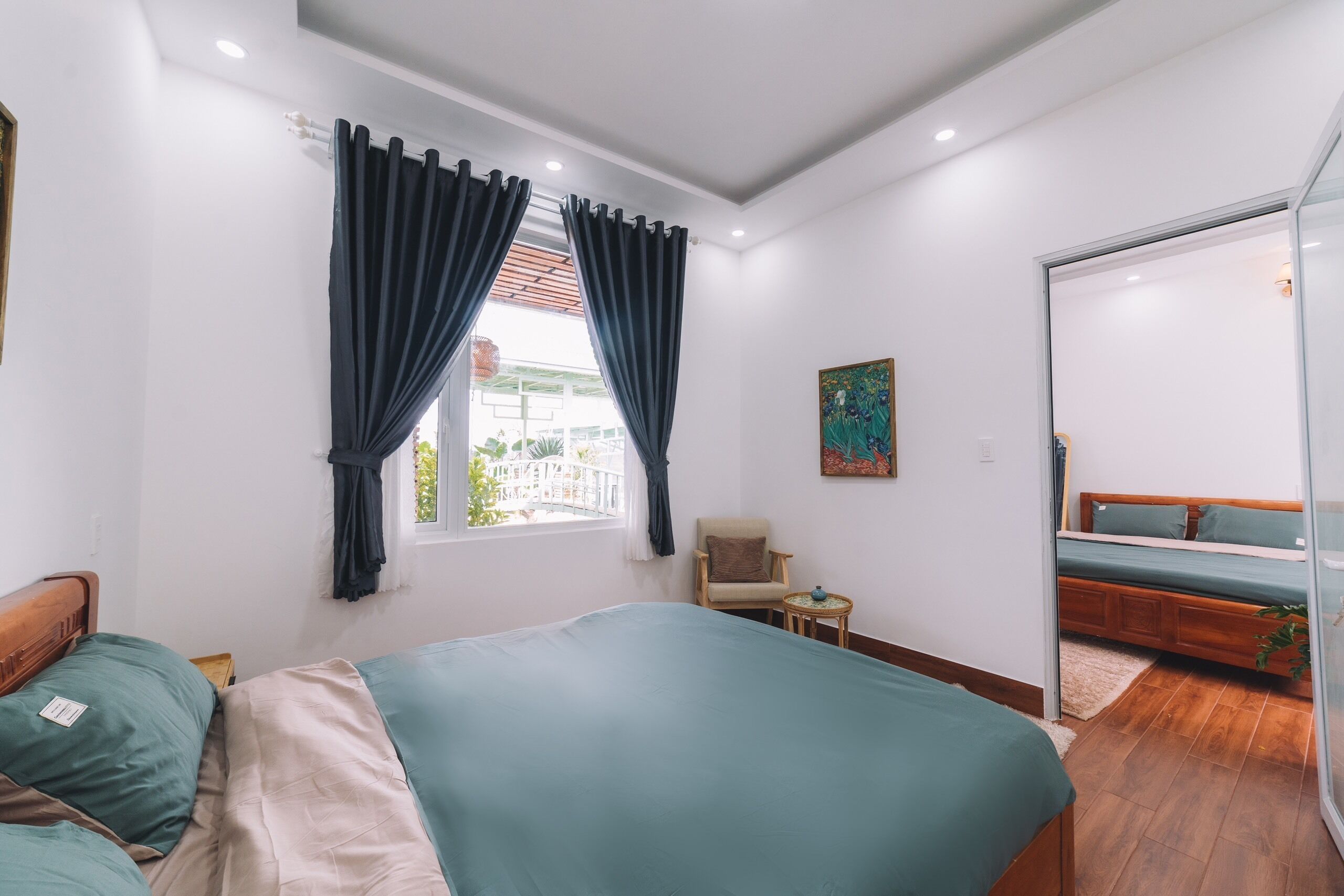 A bedroom with a large bed, a chair, a small table, and a window with curtains.