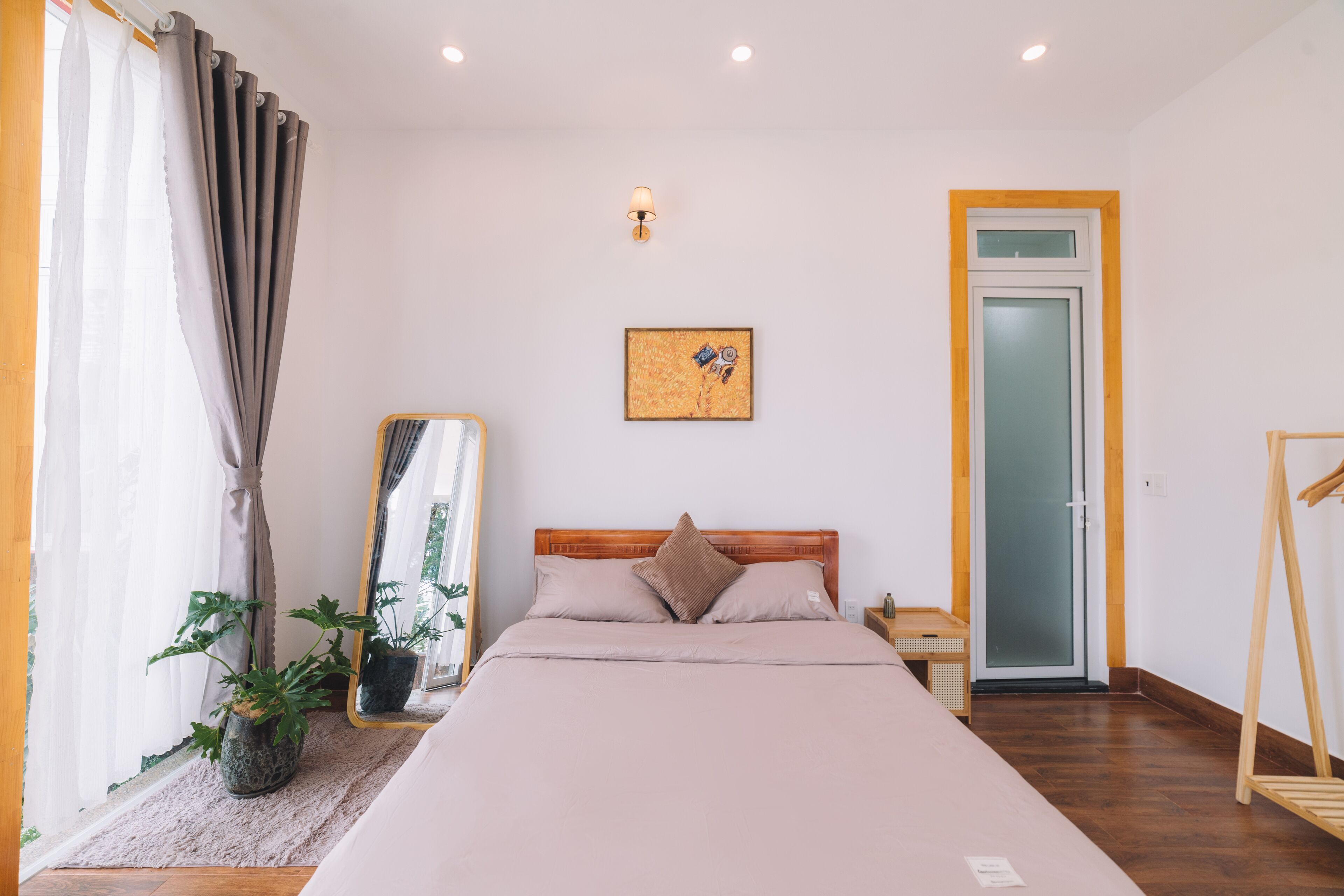 A bedroom with a bed, a bedside table, a mirror, a potted plant, and a door with a frosted glass panel.