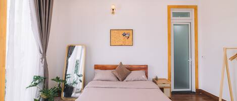 A bedroom with a bed, a bedside table, a mirror, a potted plant, and a door with a frosted glass panel.