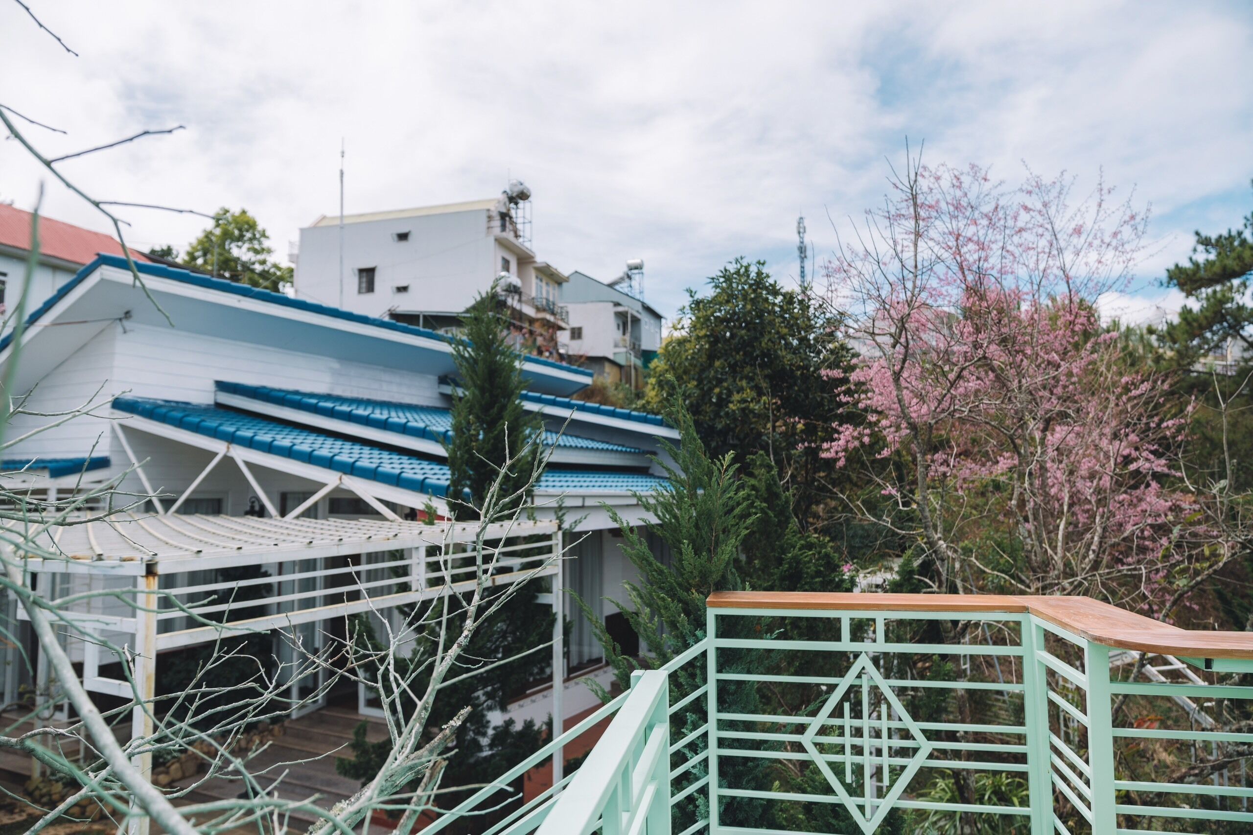 Un edificio residencial con techo azul y paredes blancas, rodeado de follaje y árboles en flor.