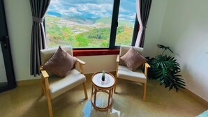 A room with a large window offering a view of terraced fields and hills. There are two chairs with cushions and a small round table. - 3 Tang May Home & Coffee (Xuan Truong - Da Lat)