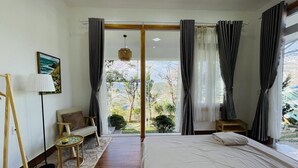 A bedroom with a large bed, a sofa, a small table, and a view of the outdoors. - 3 Tang May Home & Coffee (Xuan Truong - Da Lat)