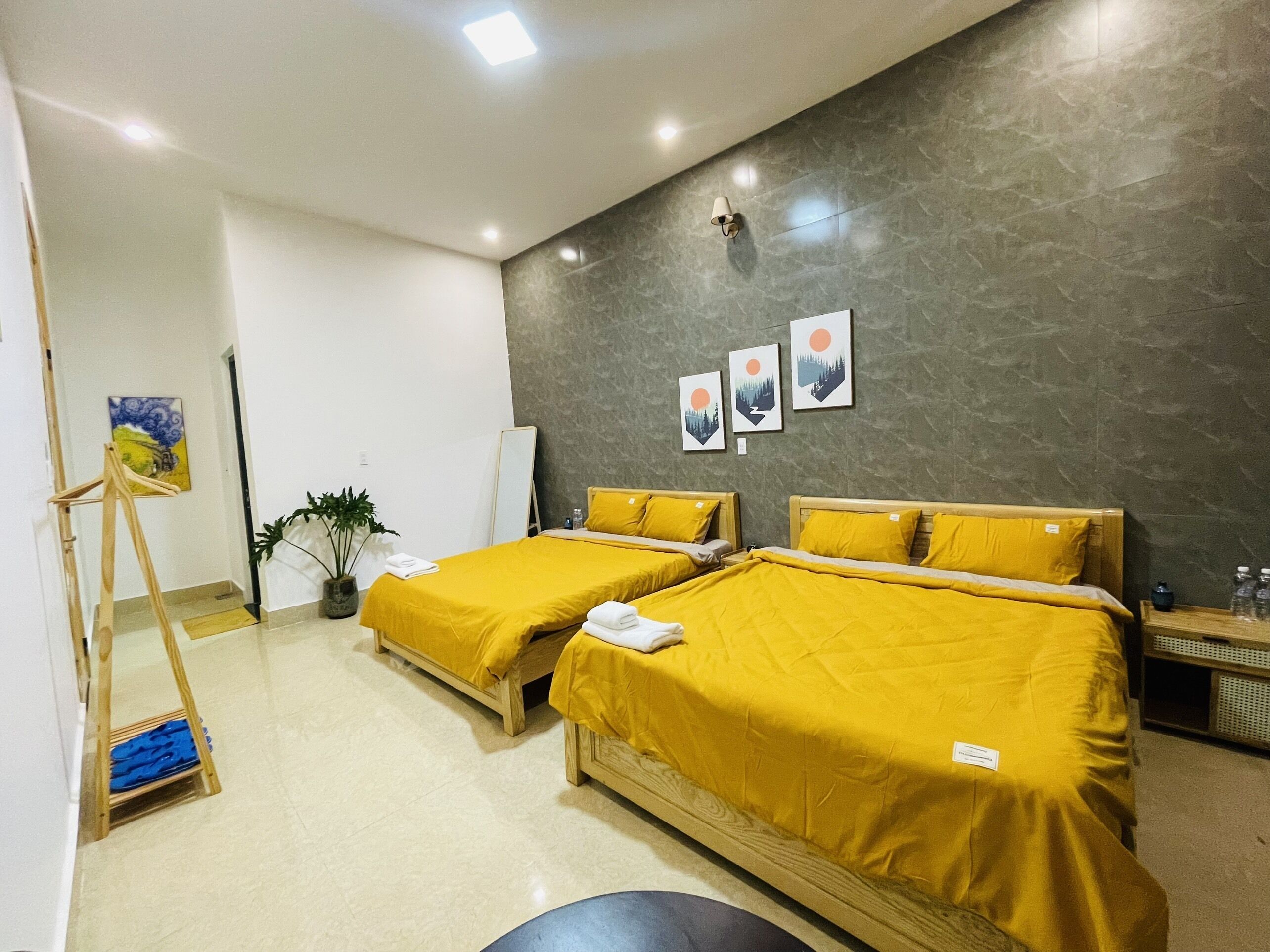 A hotel room with two beds, a standing lamp, a painting, and a small table with water bottles.