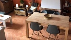 A dining area with a wooden table and chairs, a television mounted on the wall, and a large hanging lamp.