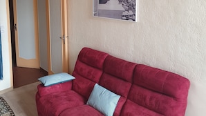 A living room with a red sofa, two patterned cushions, a framed black and white photograph on the wall, and a wooden door with a glass panel. - OLD City in Style: Bright, Spacious & Comfortable (Nice)