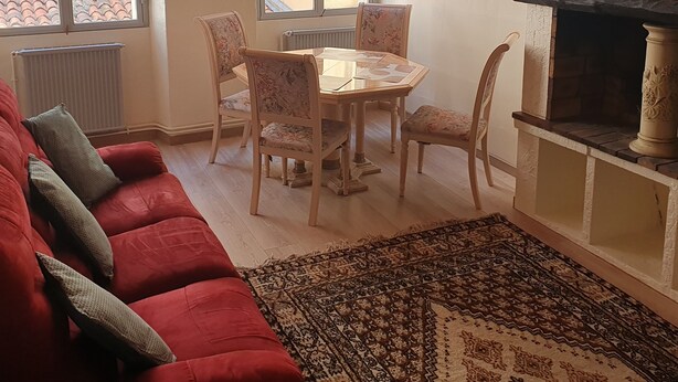 A cozy living room with a red sofa, a dining table with chairs, a fireplace, and large windows with shutters. - OLD City in Style: Bright, Spacious & Comfortable (Nice)