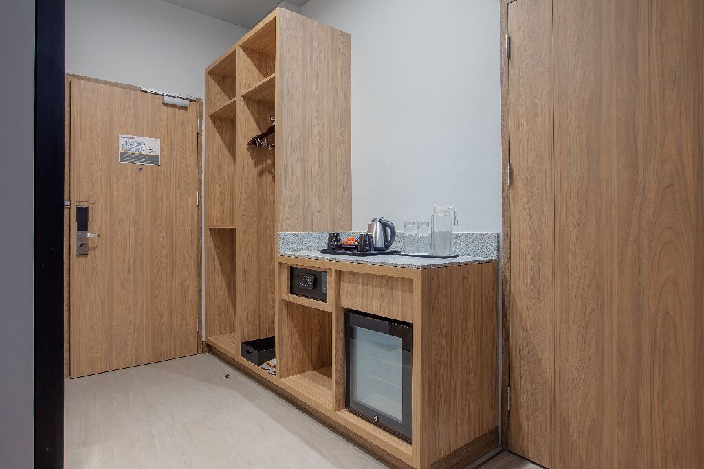 Ein kleines Zimmer mit Holzschrank, einer kleinen Küchenzeile inklusive Kaffeemaschine und einem fest installierten Fernseher.