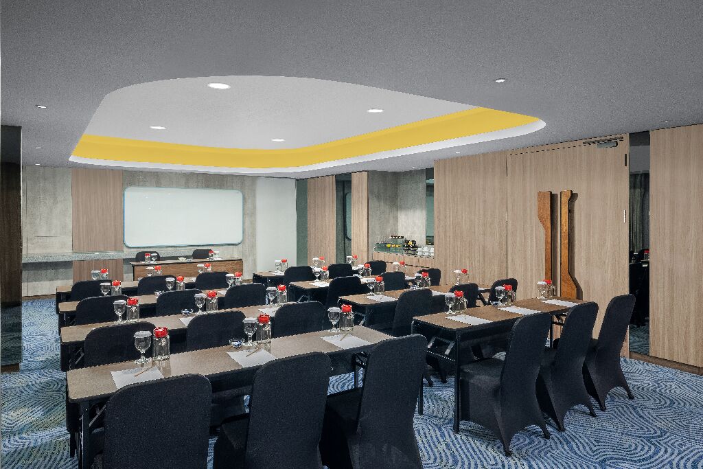 A conference room with multiple tables and chairs, a projector screen, and a presentation area.