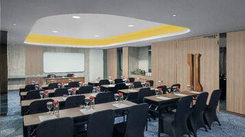 A conference room with multiple tables and chairs, a projector screen, and a presentation area.