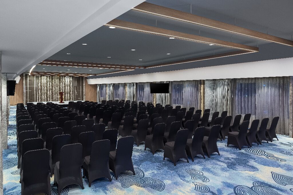 A conference room with rows of chairs, a stage, and a patterned carpet.