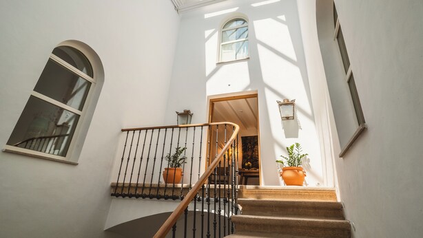 A staircase with a wooden handrail and black balusters, leading to a landing with a door and a small window. - Casa Pizarro Hotel (Cáceres)