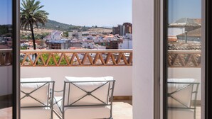 An open balcony with a view of a coastal town, a palm tree, and a tiled floor. - Casa Pizarro Hotel (Cáceres)