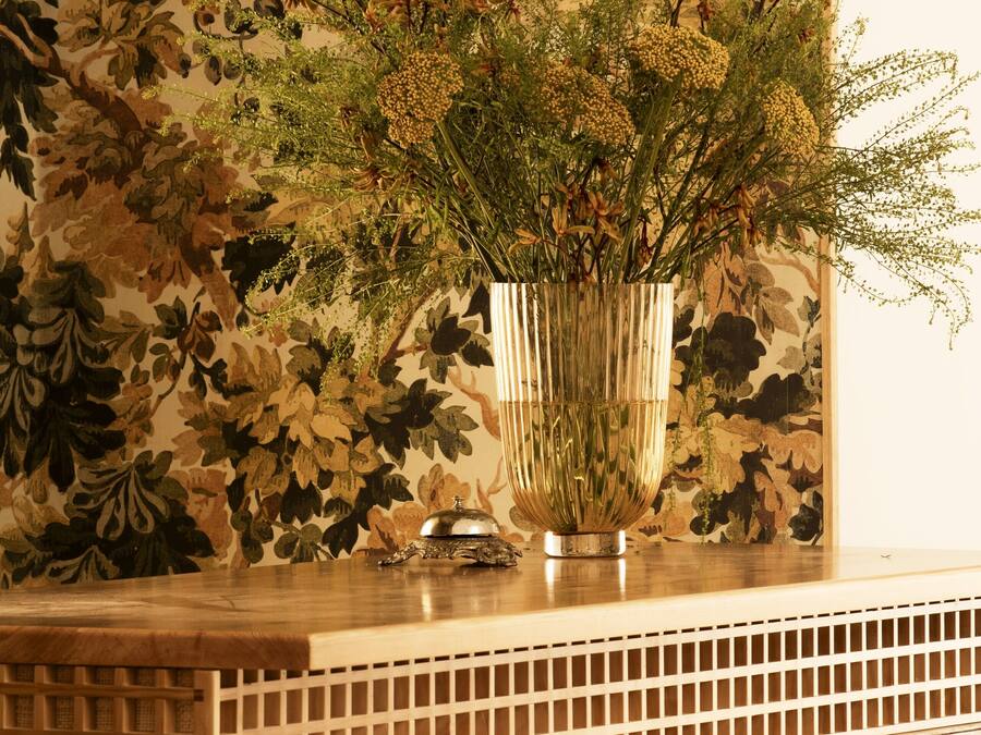 Um balcão de madeira na recepção, com um vaso de flores secas e um espelho decorativo.