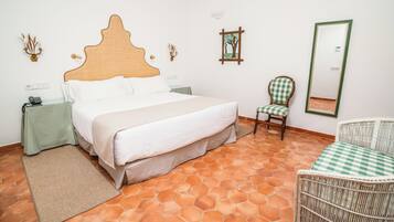 A bedroom with a large bed, a chair, a small table, and a mirror.