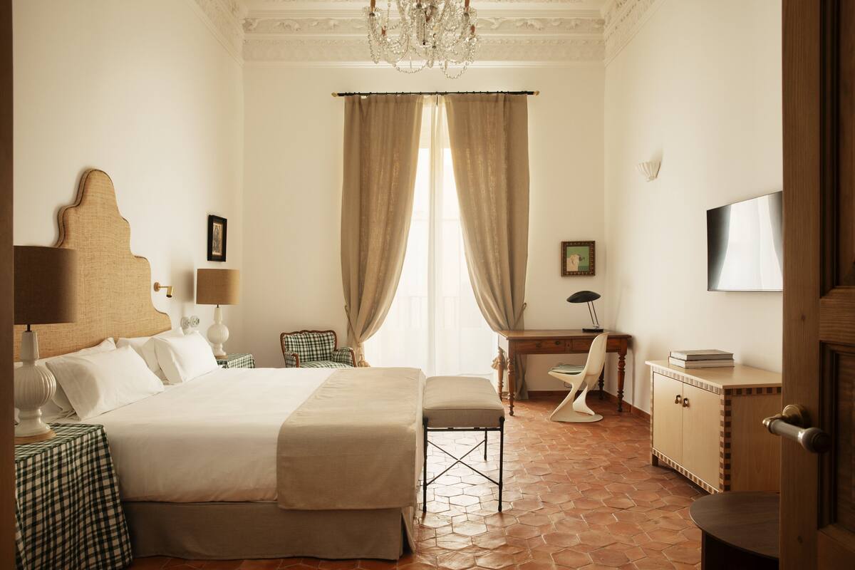 Quarto de hotel com uma cama grande, uma escrivaninha, uma cadeira, uma televisão e um guarda-roupa.