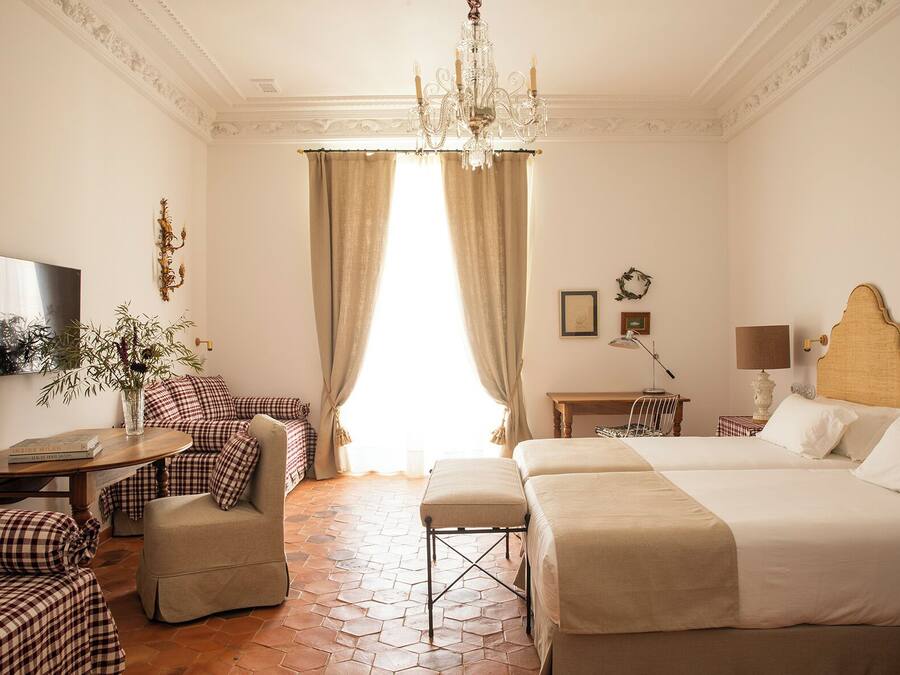 Una habitación de hotel con una cama grande, otra más pequeña, un escritorio, una silla, un sofá, un televisor y una araña.